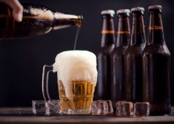 Glass bottles of beer with glass and ice on dark background
