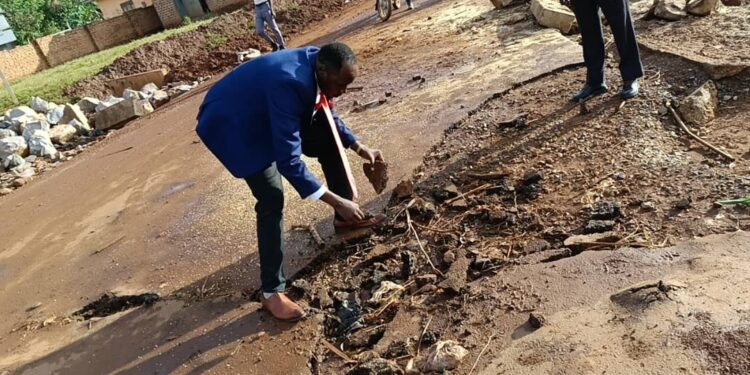 The Lugazi Central Division Chairperson, Lutajan Khemisi showing asphalt surface washed away by running water.