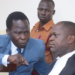 Former LRA commander Thomas Kwoyelo (in blue suit) stresses a point to his defence lawyer Boris Anyuru (R) at the Gulu High Court on August 2 2024.