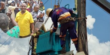 UEDCL technicians install a new transformer in Kalagi as former minister Ronald Kibuule looks on.