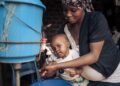Mother washing baby’s hands with clean water and soap to help prevent foodborne infections and promote good hygiene.