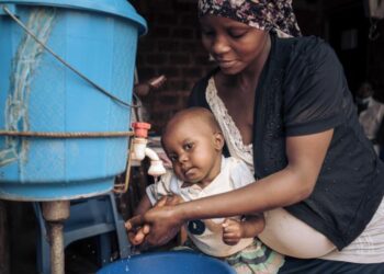 Mother washing baby’s hands with clean water and soap to help prevent foodborne infections and promote good hygiene.