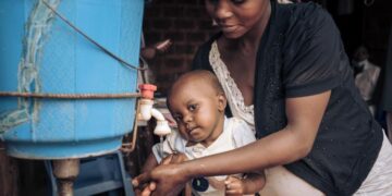 Mother washing baby’s hands with clean water and soap to help prevent foodborne infections and promote good hygiene.