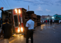 An overturned passenger bus lies on its side after colliding with a train at a railway crossing as residents gather at the scene following the crash.