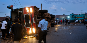 An overturned passenger bus lies on its side after colliding with a train at a railway crossing as residents gather at the scene following the crash.
