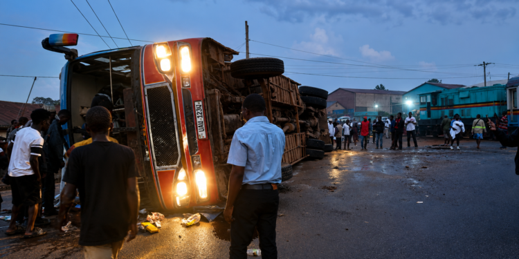 An overturned passenger bus lies on its side after colliding with a train at a railway crossing as residents gather at the scene following the crash.