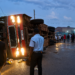 An overturned passenger bus lies on its side after colliding with a train at a railway crossing as residents gather at the scene following the crash.