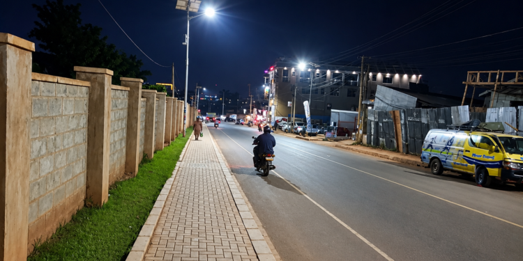 Pedestrians and motorists use a newly reconstructed, solar street lit road and paved walkway in Mukono Municipality at night. The upgraded infrastructure is intended to improve road safety, mobility, and accessibility for both motorists and pedestrians.