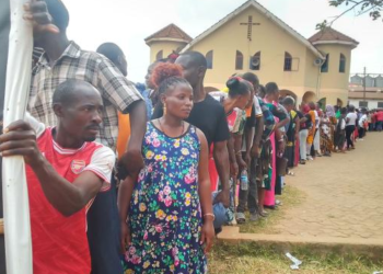 Voters line up behind a campaign banner during the Local Council elections.