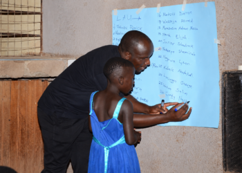 Diphas Kiguli, Board Vice Chairperson of Literacy Aid Uganda, practically conducts registration with some of the children during a community literacy outreach programme in Benghazi Ghetto Community, Kitega-Anthony Cell, Mukono Municipality.