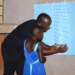 Diphas Kiguli, Board Vice Chairperson of Literacy Aid Uganda, practically conducts registration with some of the children during a community literacy outreach programme in Benghazi Ghetto Community, Kitega-Anthony Cell, Mukono Municipality.