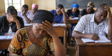 Adult learners attend a lesson in a modest classroom. Thirteen learners in Kawempe, Kampala, reportedly missed the 2026 UCE examinations after discovering they had not been registered. The image is illustrative.
