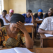 Adult learners attend a lesson in a modest classroom. Thirteen learners in Kawempe, Kampala, reportedly missed the 2026 UCE examinations after discovering they had not been registered. The image is illustrative.
